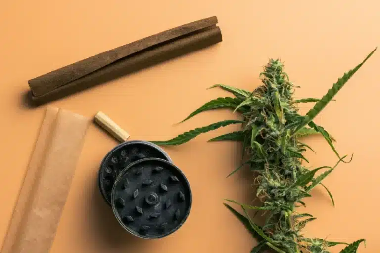 An herb grinder, a pre-rolled joint, and cannabis flower on top of an orange table.