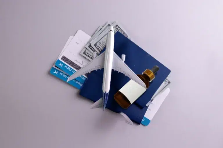 an artistic arrangement of a little plastic plane and passport with money and a bottle of CBD oil.