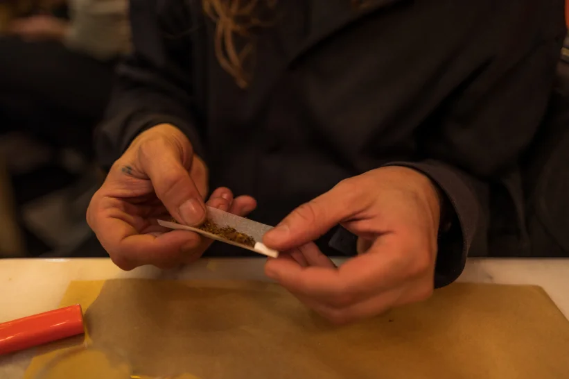 a person rolling a piece of paper with ground sativa weed inside