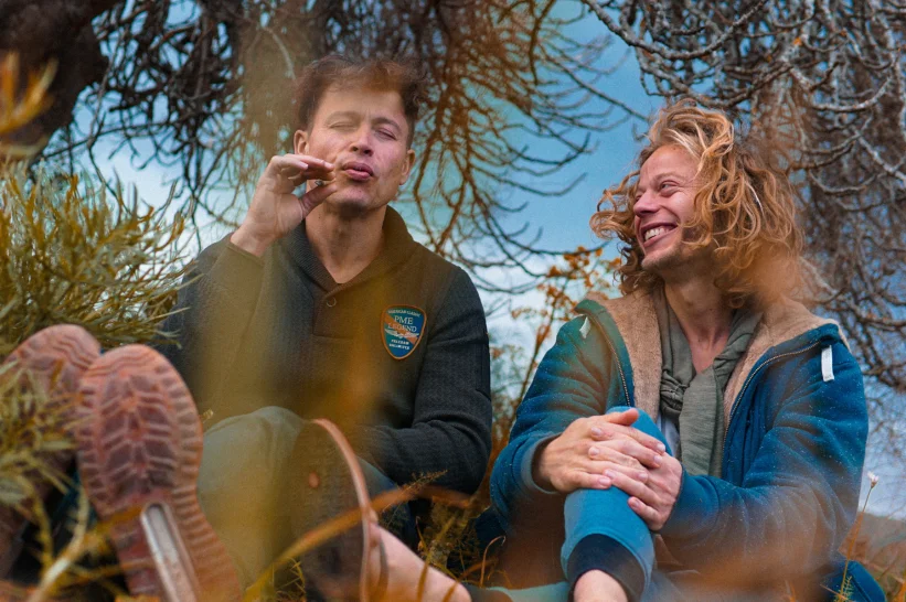 two men sitting outside in the grass enjoying the effects of Sativa strains