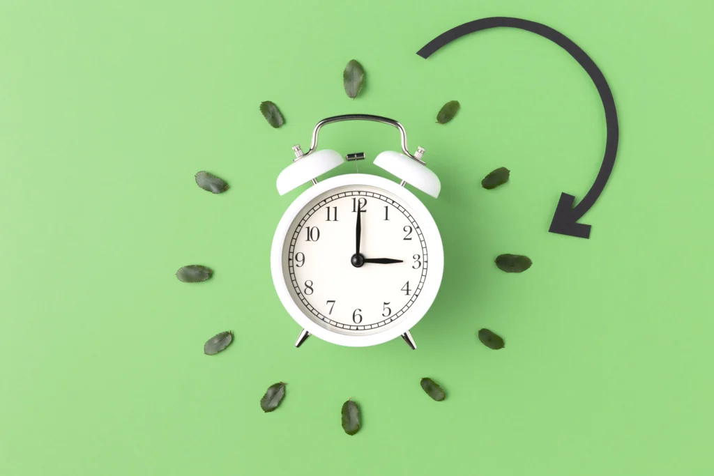 a white alarm clock with a black arrow and leaves around it