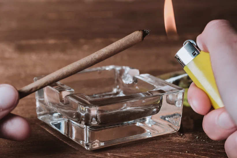 a hand holding a lighter and a blunt in a glass ashtray