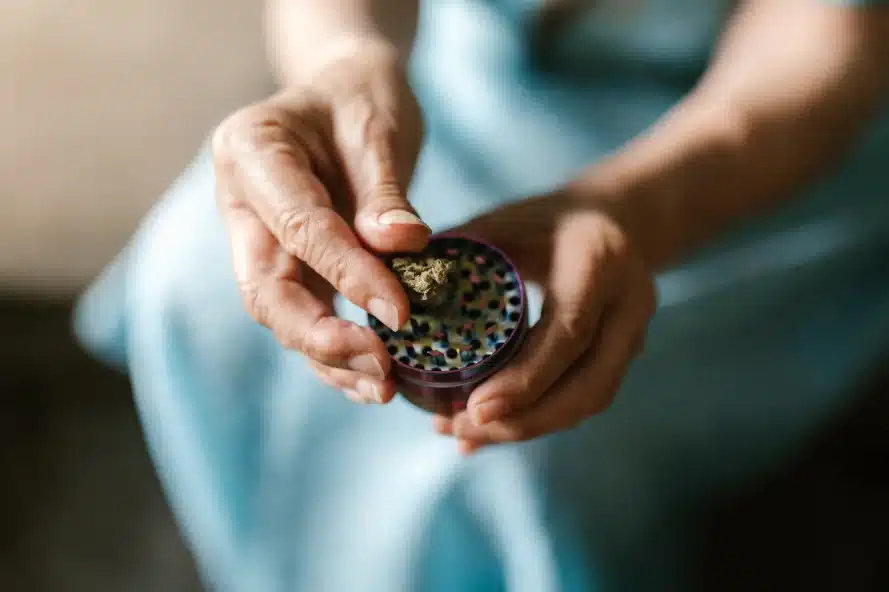 a person holding a grinder with bits of cannabis