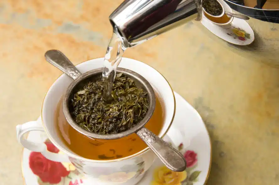 a tea cup with a silver strainer and a silver teapot
