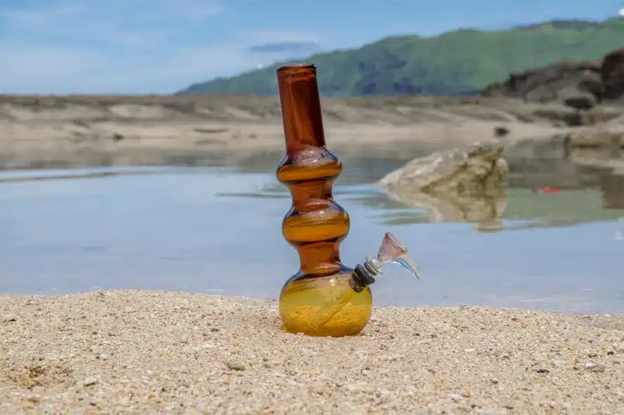 a glass bong on sand near water