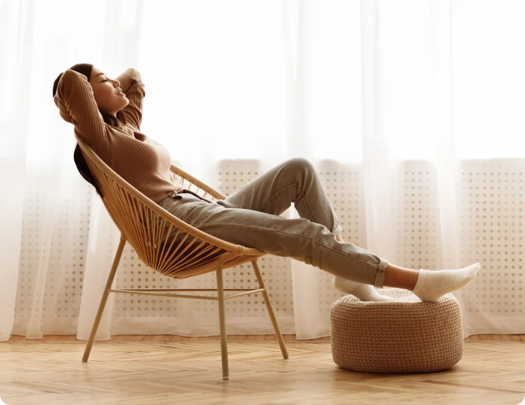 Woman relaxing in a wicker chair with her feet up beside a sunlit window