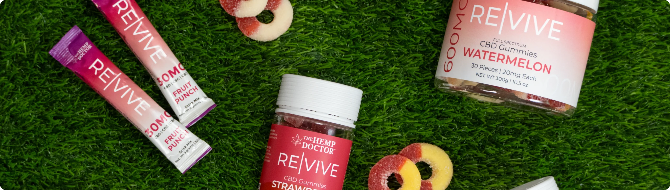 Re|Vive CBD gummies and drink mix packets from The Hemp Doctor laid out on grass