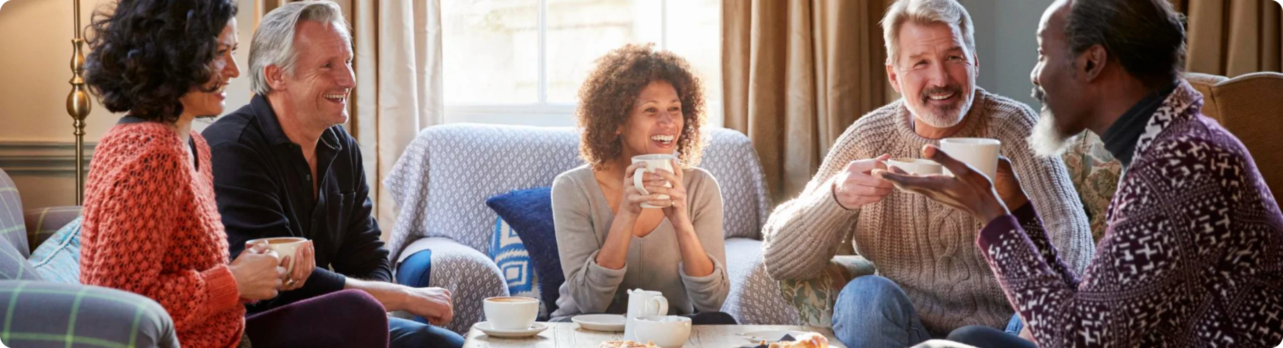A group of friends laughing together over coffee on a living-room sofa