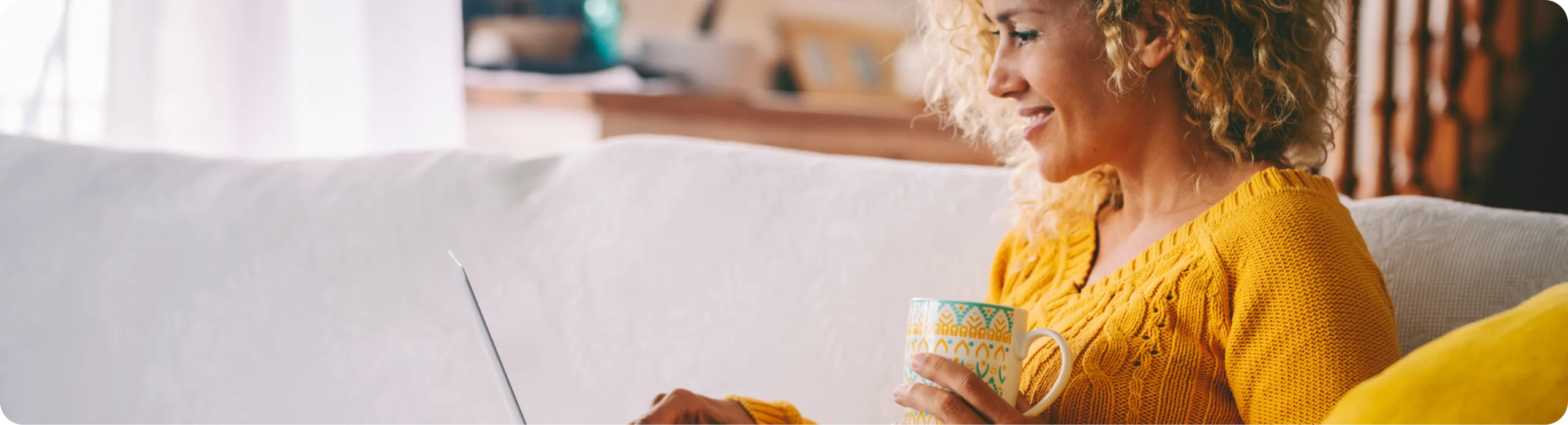 A woman relaxing on a sofa with a laptop and a mug of tea