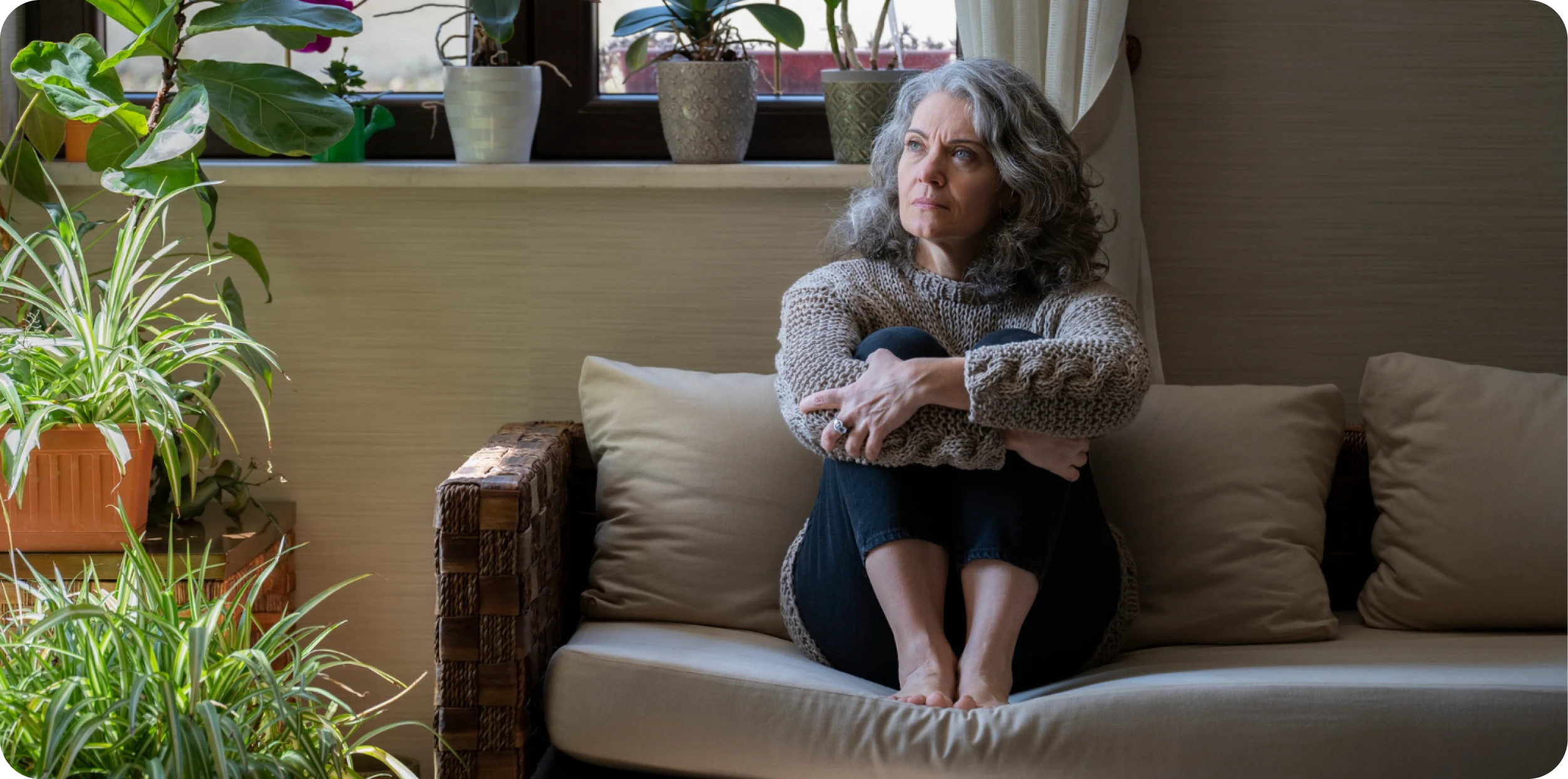 A woman resting on a sofa surrounded by houseplants